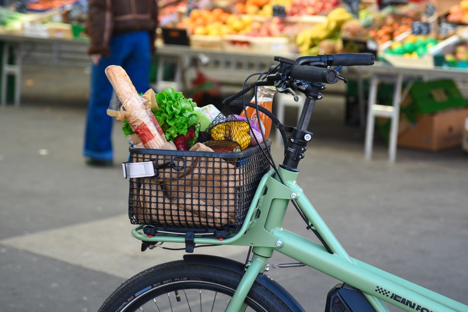 An e-bike with a loaded basket of groceries at a vibrant outdoor market in France.