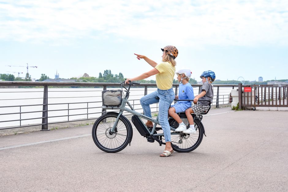 A woman and two children explore the Bordeaux riverfront on an E-bike, enjoying a summer day.